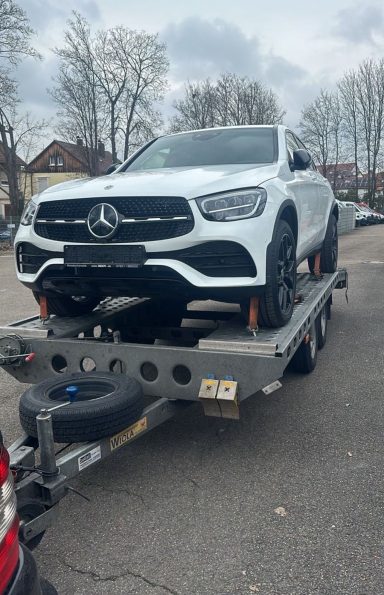 Weißer Mercedes GLC auf einem Anhänger, geparkt auf einer Straße.